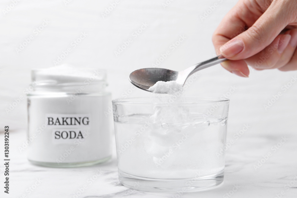 Woman adding baking soda to glass of water at white marble table, closeup Woman adding baking soda to glass of water at white marble table, closeup