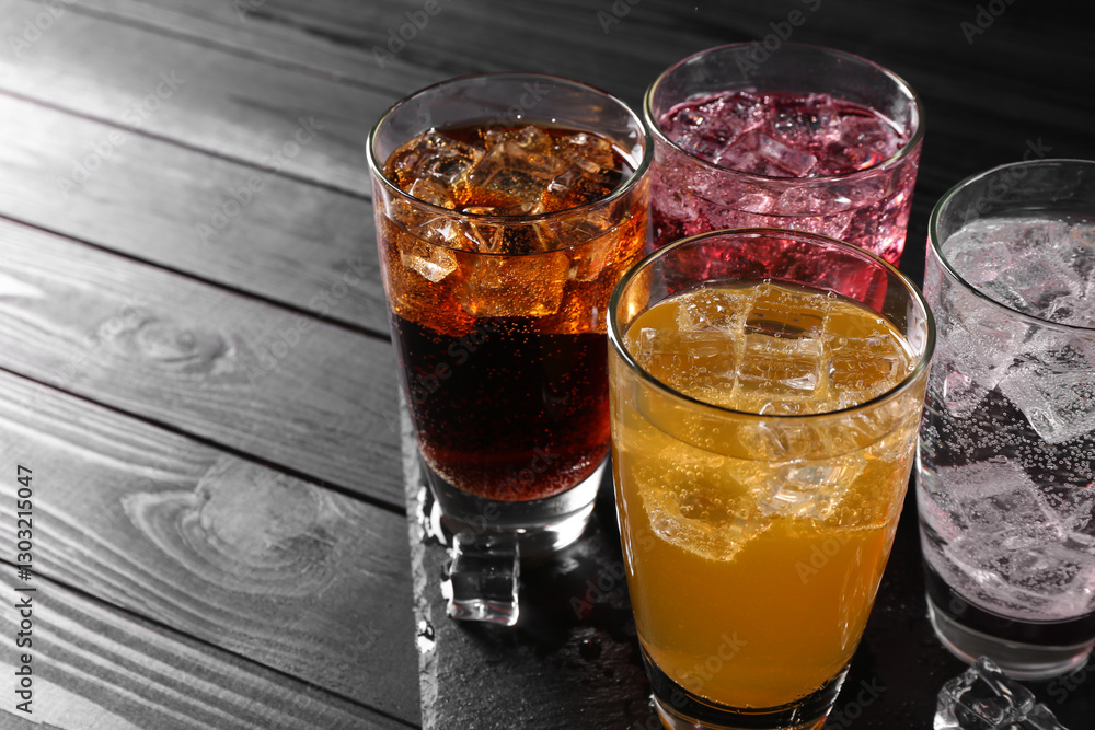 Refreshing soda water of different flavors in glasses with ice cubes on black wooden table, space for text Refreshing soda water of different flavors in glasses with ice cubes on black wooden table, space for text