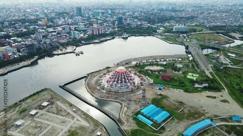 The atmosphere of the construction of Losari Beach and the 99-dome mosque with the backdrop of the cityscape on a sunny day and clear sea.