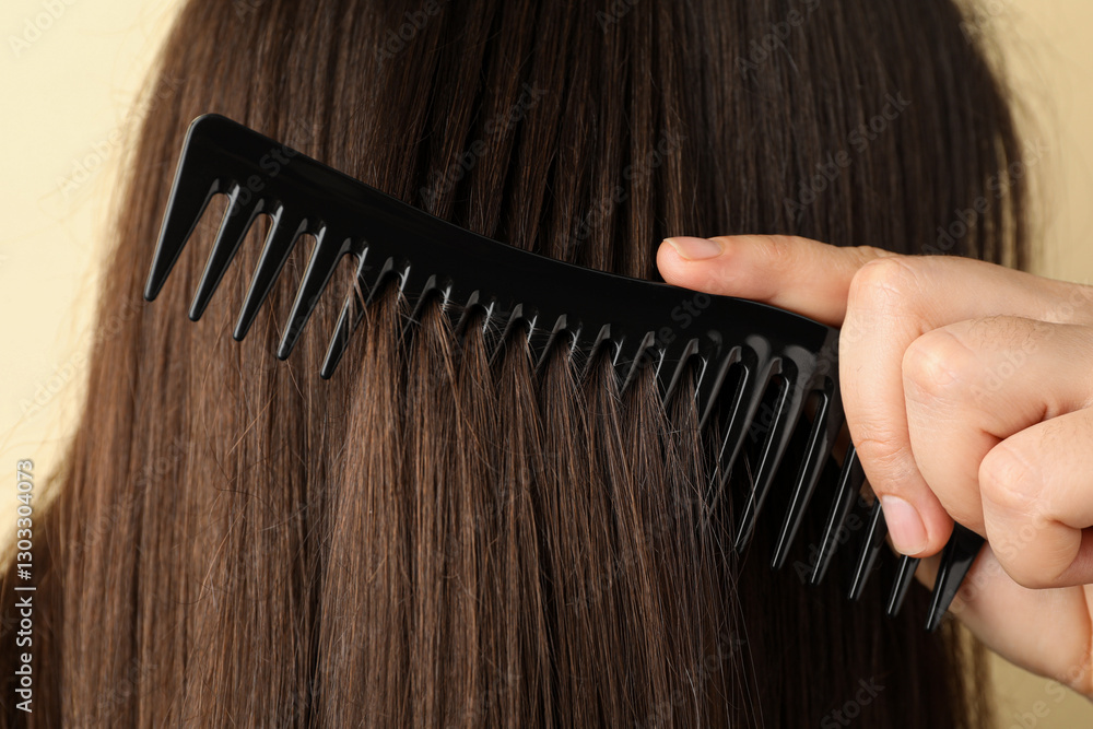 Obraz premium Woman brushing hair with plastic comb on beige background, closeup