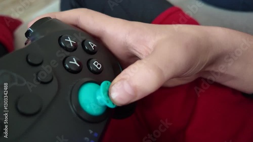 A child's hand moves quickly on a video game controller, pressing buttons and joysticks. The child's face is not shown.