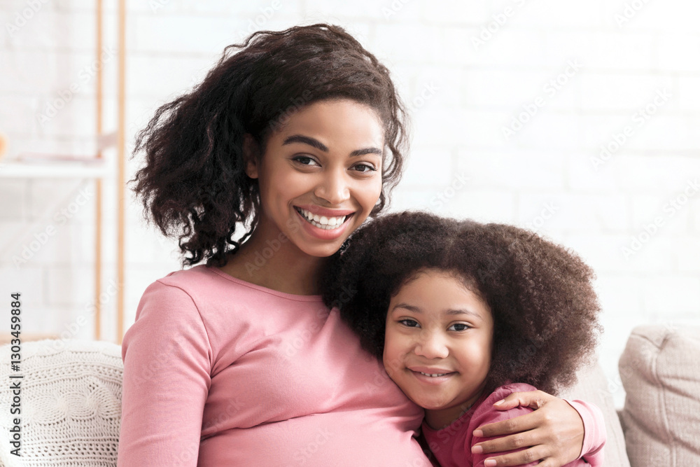 Pregnant Mother And Child. Portrait of happy expecting afro woman hugging with her cute little daughter at home and looking at camera, copy space Pregnant Mother And Child. Portrait of happy expecting afro woman hugging with her cute little daughter at home and looking at camera, copy space