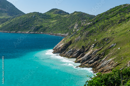 View of Guriri cove turquoise waters surrounded by Pontal do Atalaia mountains fully covered by lush dense green vegetation under summer morning blue sky in Arraial do Cabo, Rio de Janeiro - Brazil.