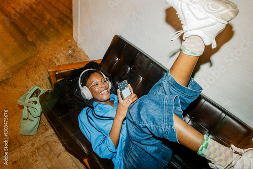 High angle view of happy female entrepreneur listening to music while lying down on sofa at office