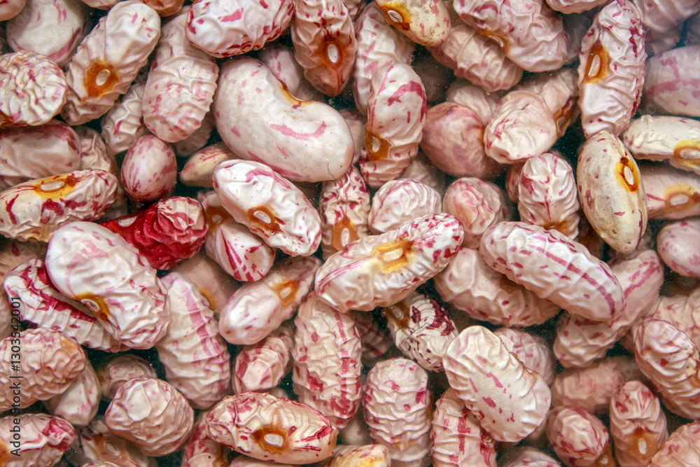A collection of wrinkled, pink and cream colored beans. Their varying shades and textures suggest natural irregularities,creating an intricate visual pattern.Pinto beans soaked in water, ready to eat. A collection of wrinkled, pink and cream colored beans. Their varying shades and textures suggest natural irregularities,creating an intricate visual pattern.Pinto beans soaked in water, ready to eat.