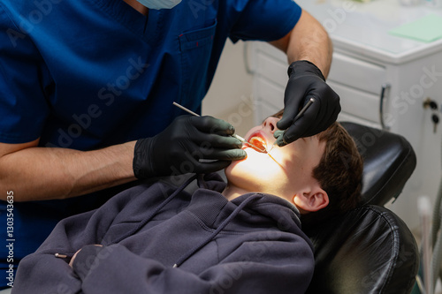 A dentist checks the teeth of a child who is sitting in an armchair with his mouth wide open. Routine dental check-up. Health