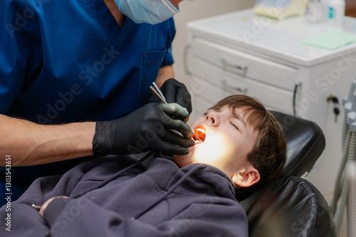 A dentist checks the teeth of a child who is sitting in an armchair with his mouth wide open. Routine dental check-up. Health
