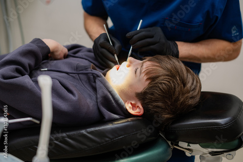 A dentist checks the teeth of a child who is sitting in an armchair with his mouth wide open. Routine dental check-up. Health