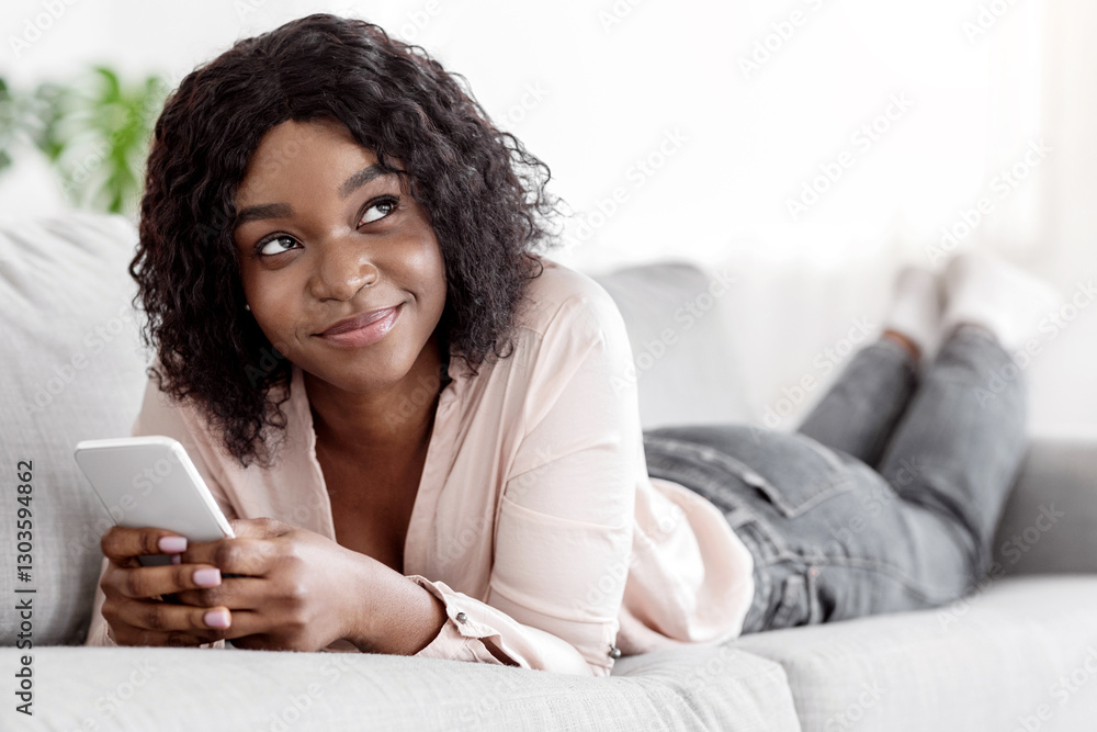 Pensive african woman using smartphone while lying on comfy sofa at home, resting in living room, texting with friends, enjoying online communication, looking away, thinking about message, closeup Pensive african woman using smartphone while lying on comfy sofa at home, resting in living room, texting with friends, enjoying online communication, looking away, thinking about message, closeup
