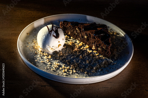 White ice cream scoop on dark plate with chocolate and nut decoration