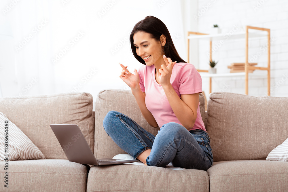 Cherished Wish. Portrait of young woman pleading for something with crossed fingers, using laptop sitting on couch Cherished Wish. Portrait of young woman pleading for something with crossed fingers, using laptop sitting on couch