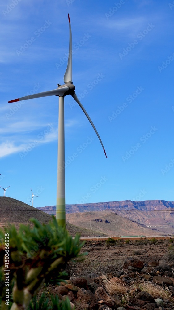 Wind turbine generating clean energy in a volcanic landscape with mountains and vegetation in the Canary Islands, under a blue sky with some clouds
