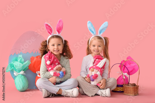 Cute little girls in bunny ears with gnomes and Easter eggs sitting on pink background