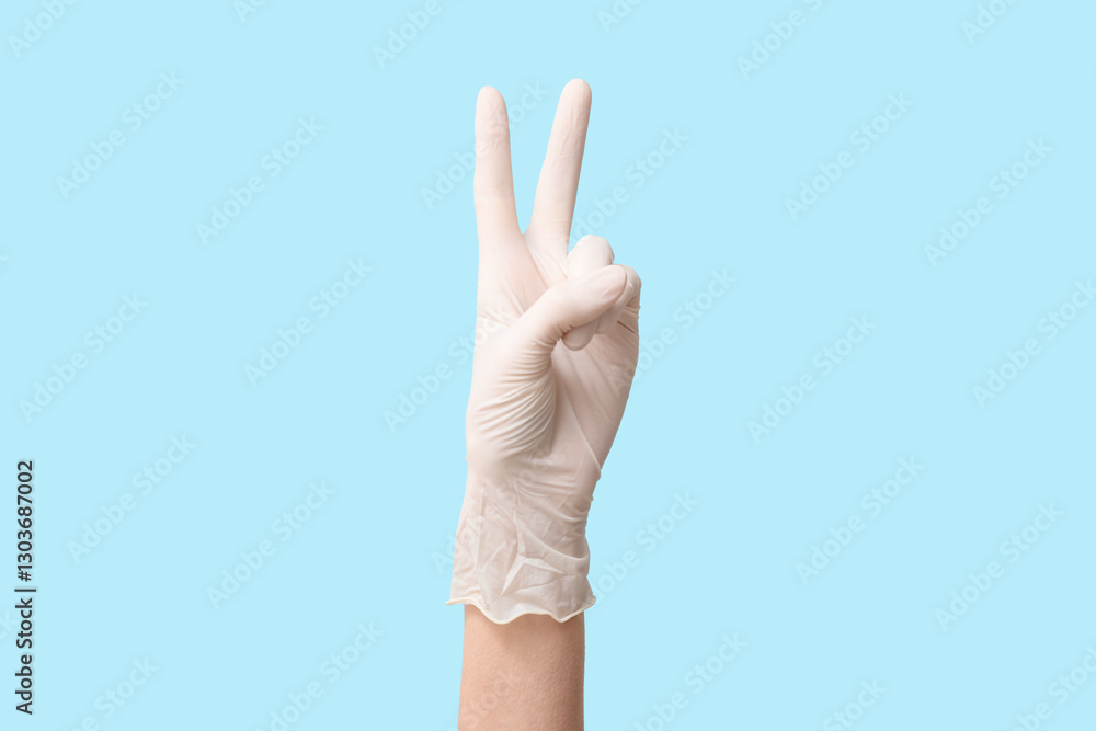 Naklejka premium Female hand in medical glove showing victory gesture on blue background