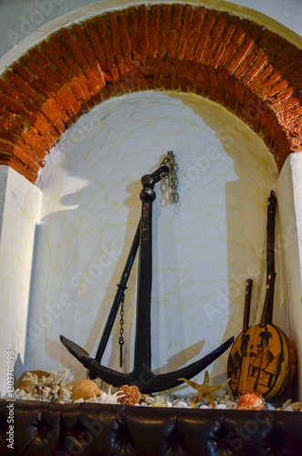 A nautical display in a brick alcove, featuring a large anchor, a stringed instrument, and seashells. A cozy, marine-themed interior decoration.