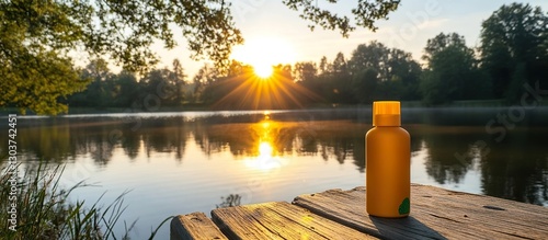 An eco-friendly sunscreen bottle on a wooden dock by the serene lake, surrounded by natural beauty, with trees and the sun reflecting on the water.