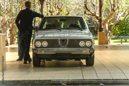 Relic of an old car on display with the composition of a man with his back turned leaning against the car seen from the front with the beautiful headlights and grille