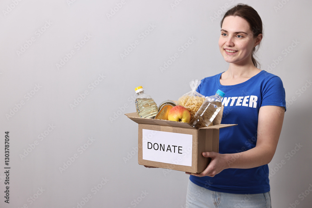 Woman holding donation box with food products on grey background, space for text Woman holding donation box with food products on grey background, space for text