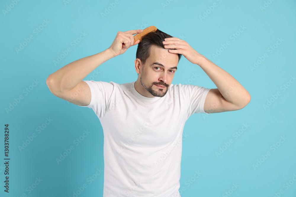 Fototapeta premium Handsome man stylish his hair with comb on light blue background