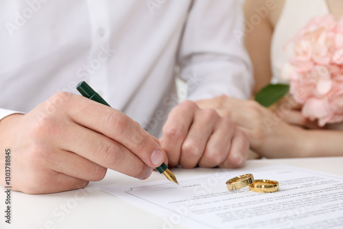 Фотография Newlyweds signing marriage contract and wedding rings on desk, selective focus