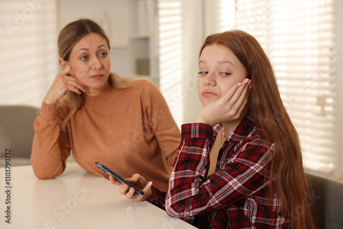 Annoyed teenage girl with smartphone and her mother at psychologist's office, selective focus