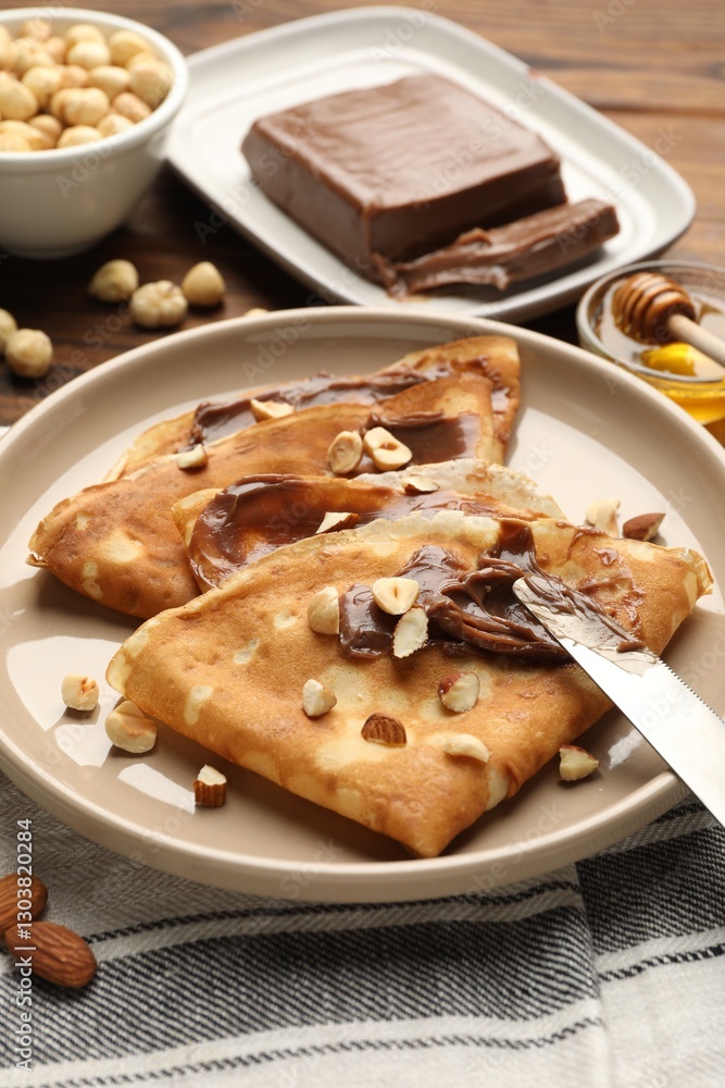 Tasty crepes with chocolate butter, nuts, honey and knife on table, closeup Tasty crepes with chocolate butter, nuts, honey and knife on table, closeup