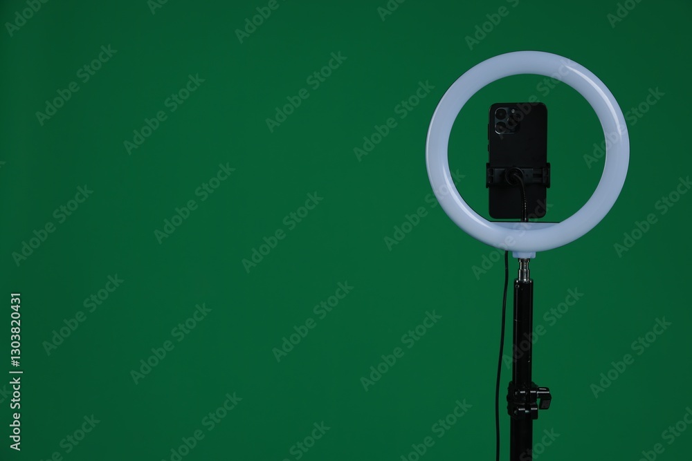 Ring lamp with smartphone on green background, space for text