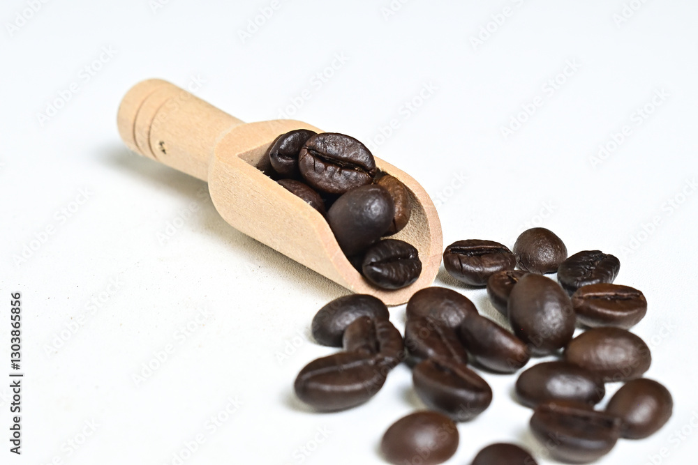 Obraz premium Close up view of roasted coffee beans in little wooden scoop with roasted coffee beans around it isolated on white background. Clipping path.