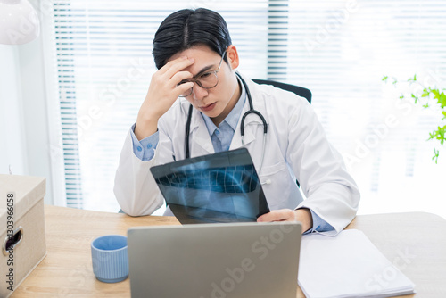 Fotografi Young Asian doctor reviewing medical x-ray in a well-lit office while expressing