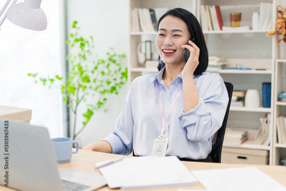 Smiling woman engages in a phone conversation while working at her desk in a modern office environment Smiling woman engages in a phone conversation while working at her desk in a modern office environment