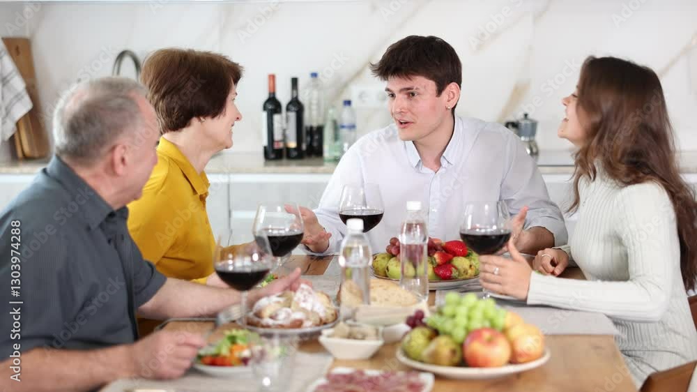Senior man at kitchen table with wife, grown son and daughter, enjoying conversation at festive table with wine and light snacks Senior man at kitchen table with wife, grown son and daughter, enjoying conversation at festive table with wine and light snacks