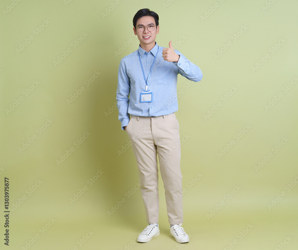 Young man in business attire gives thumbs up against a light green background Young man in business attire gives thumbs up against a light green background