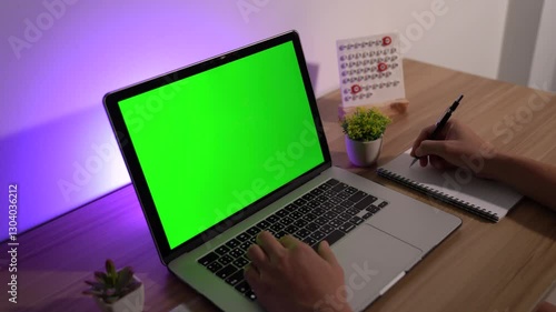 Laptop with Green Screen: Person working on a laptop with a green screen, a desk with a pen, notepad, calendar, and decorative plant, evoking the scene of productivity and modern work