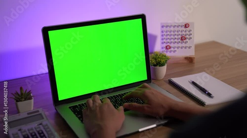 Workspace with Laptop and Calendar: A modern workspace featuring a laptop with a vibrant green screen, hands typing on the keyboard, a calendar, a notepad.