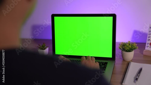 Green Screen Laptop: A person working at a desk with a laptop displaying a vibrant green screen, perfect for showcasing digital content or mockups. 