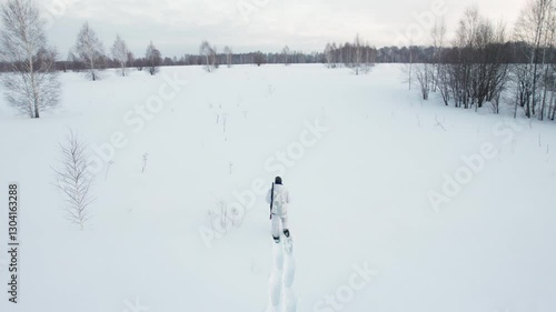 Hunter in snowshoes and winter camouflage walking across the field