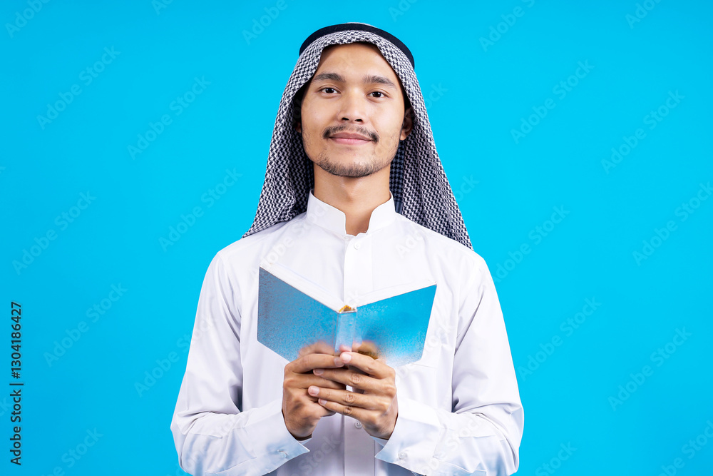 Portrait Of Young Muslim Man Smiling While Holding Holy Qur'an Isolated On Blue Background Portrait Of Young Muslim Man Smiling While Holding Holy Qur'an Isolated On Blue Background