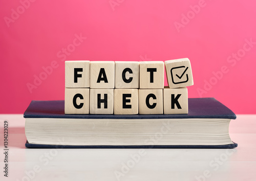 Cuadro en lienzo Wooden cubes showing fact check on a book with pink background
