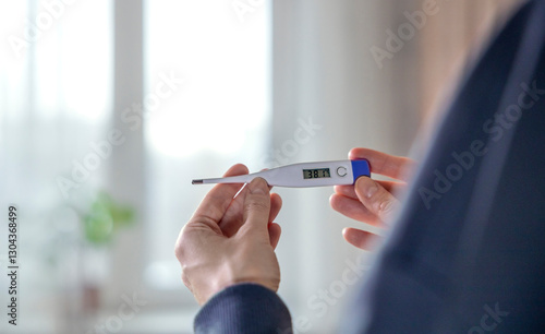 Woman holding a thermometer at home measuring high temperature photo