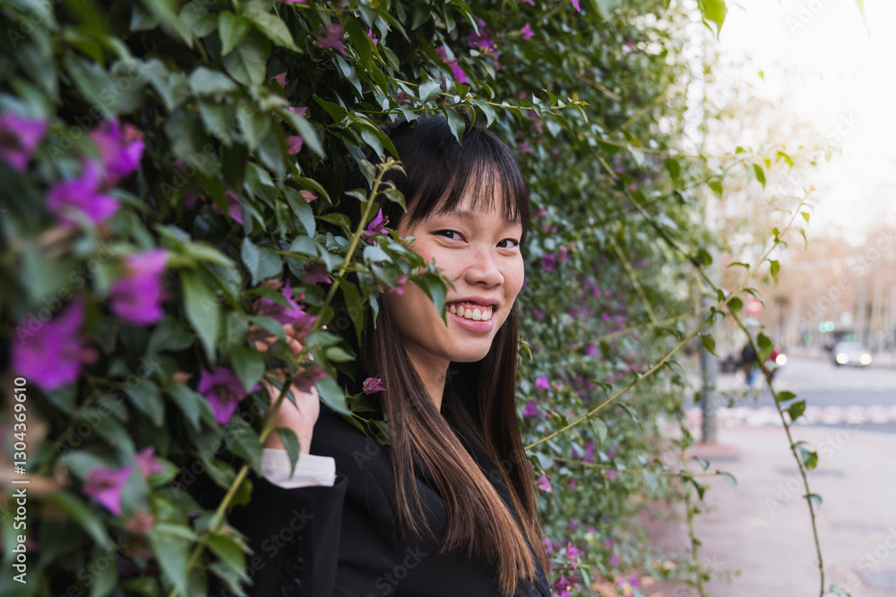 Smiling woman leaning against wall with flowering bush Smiling woman leaning against wall with flowering bush