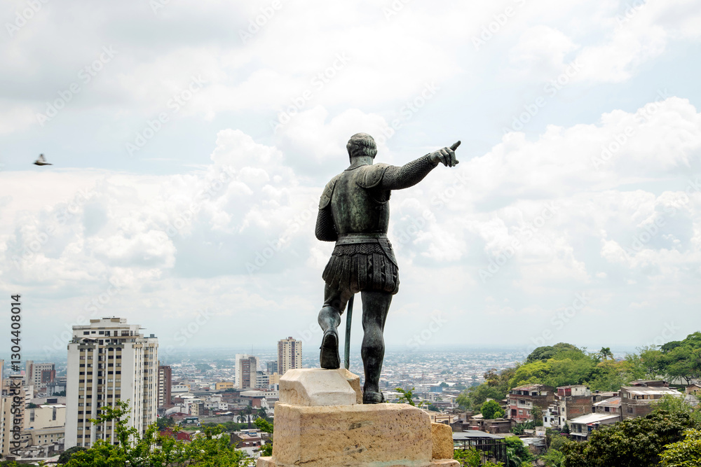 Fototapeta premium Statue of Sebastián de Belalcázar at the top of a viewpoint, with a panoramic view of the city of Cali, Colombia. He points with his right hand towards the horizon. In the background, 