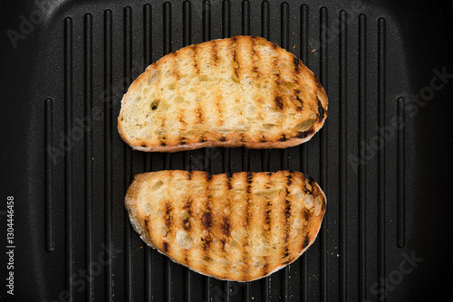 Toasted slices of ciabatta lie on a grill pan