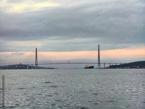 The russky bridge stretches across the calm sea during sunset in vladivostok. the sky's gentle hues add a serene backdrop to the impressive cable-stayed structure, while ships navigate the tranquil