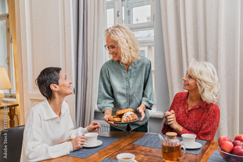 Three elderly women sitting at table chatting joyfully. Elegance blonde senior women chill together talking. Female aged friends having tea time at home and communicating smiling Three elderly women sitting at table chatting joyfully. Elegance blonde senior women chill together talking. Female aged friends having tea time at home and communicating smiling