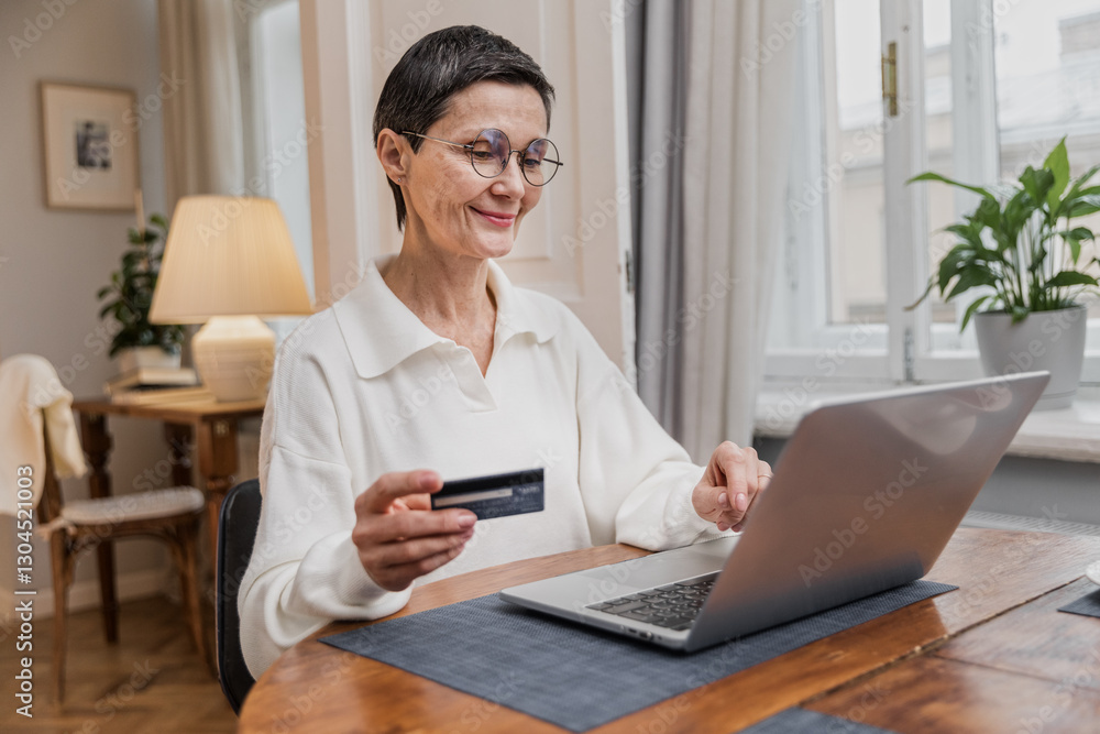 Senior elegant woman sits at table typing doing online shopping. Cheerful aged female makes purchase using laptop. Older focused paying for order by credit card online. Senior elegant woman sits at table typing doing online shopping. Cheerful aged female makes purchase using laptop. Older focused paying for order by credit card online.