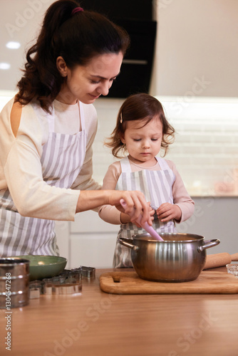 mother and her little child daughter in aprons preparing the dough in the kitchen, bake cookies