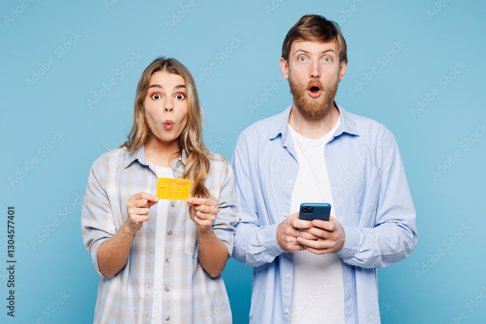 Young surprised couple two friends family man woman wear shirt casual clothes using mobile cell phone hold credit bank card shopping online order delivery book tour isolated on plain blue background. Young surprised couple two friends family man woman wear shirt casual clothes using mobile cell phone hold credit bank card shopping online order delivery book tour isolated on plain blue background.