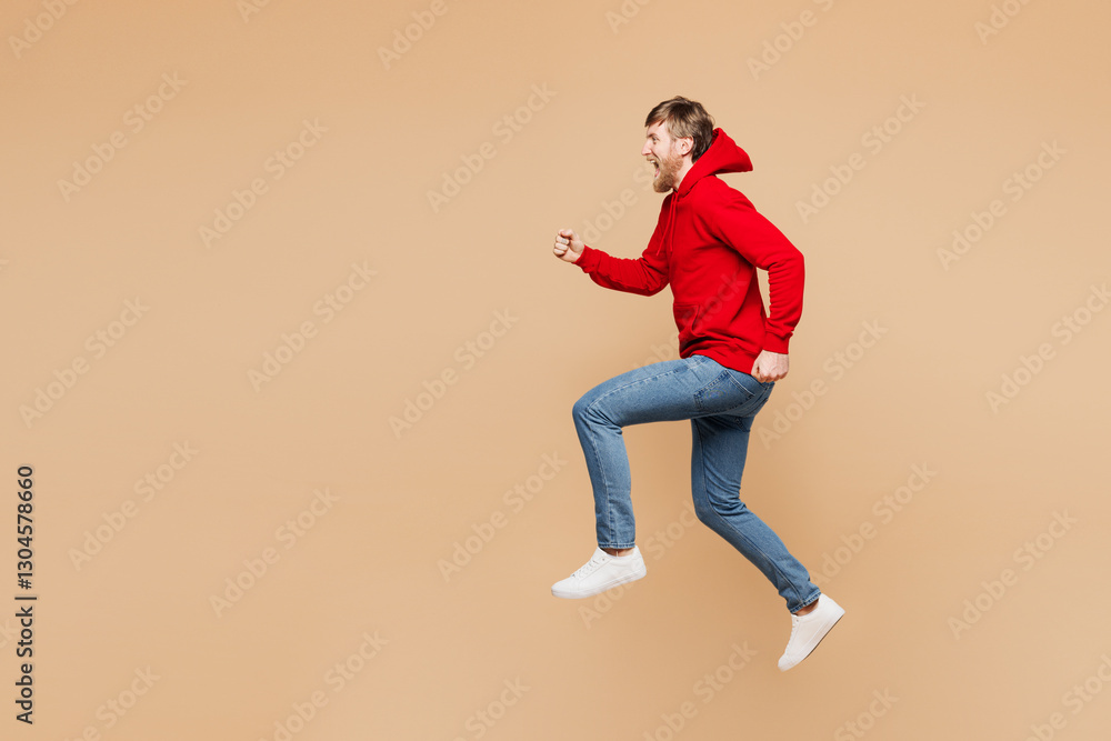 Full body side profile view young happy Caucasian man he wear red hoodie casual clothes jump high run fast hurry up isolated on pastel plain light beige background studio portrait. Lifestyle concept. Full body side profile view young happy Caucasian man he wear red hoodie casual clothes jump high run fast hurry up isolated on pastel plain light beige background studio portrait. Lifestyle concept.