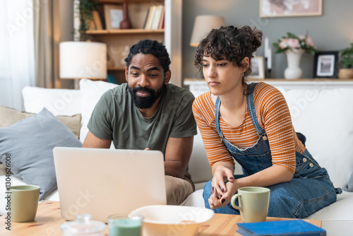 Relationship difficulties, communication problems. Young couple sitting at home having online therapy with psychotherapist on video call on laptop computer. Man and woman talking to therapist.