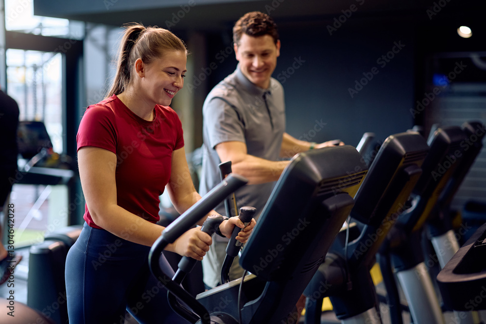 Happy athletic woman exercising on elliptical machine during sports training with fitness instructor at health club. Happy athletic woman exercising on elliptical machine during sports training with fitness instructor at health club.